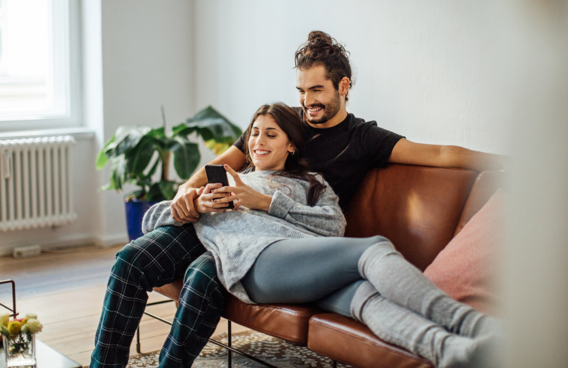 Ein Pärchen sitzt bzw. liegt auf dem Sofa und beide schauen gemeinsam auf ein Smartphone. Ein Pärchen sitzt bzw. liegt auf dem Sofa und beide schauen gemeinsam auf ein Smartphone.